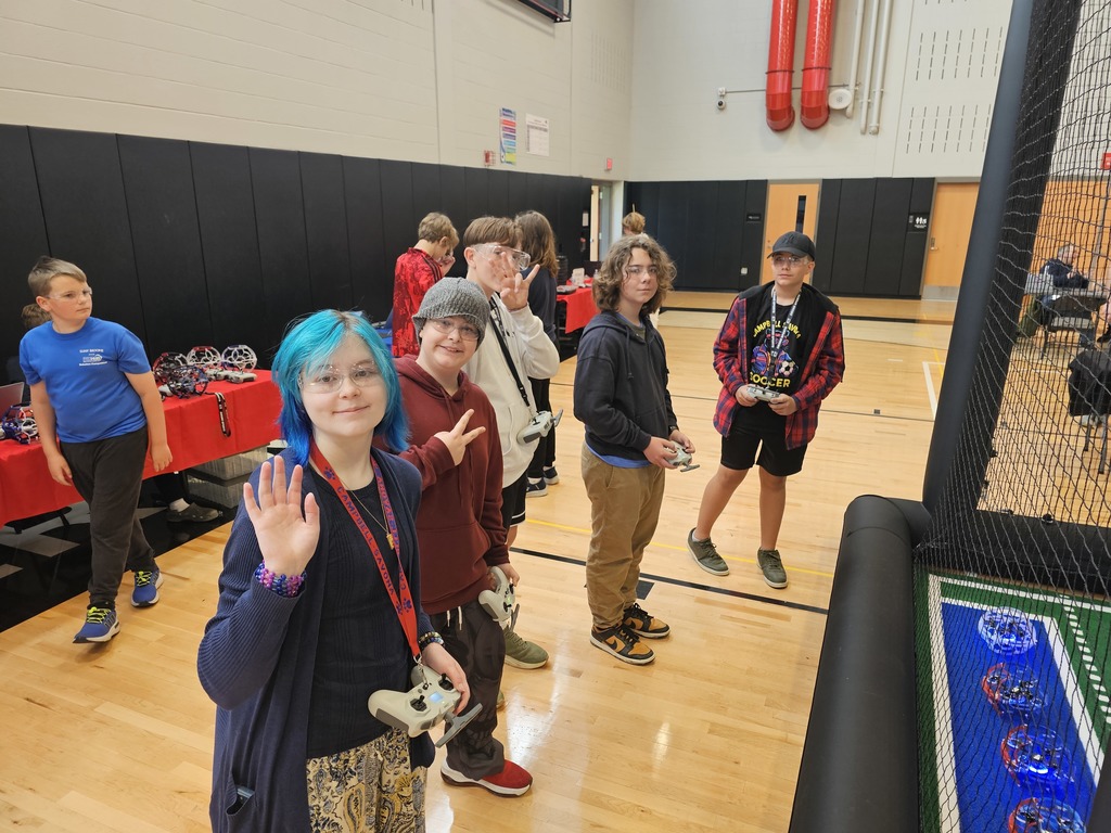 Students standing in front of the drone soccer arena with controllers smiling for camera