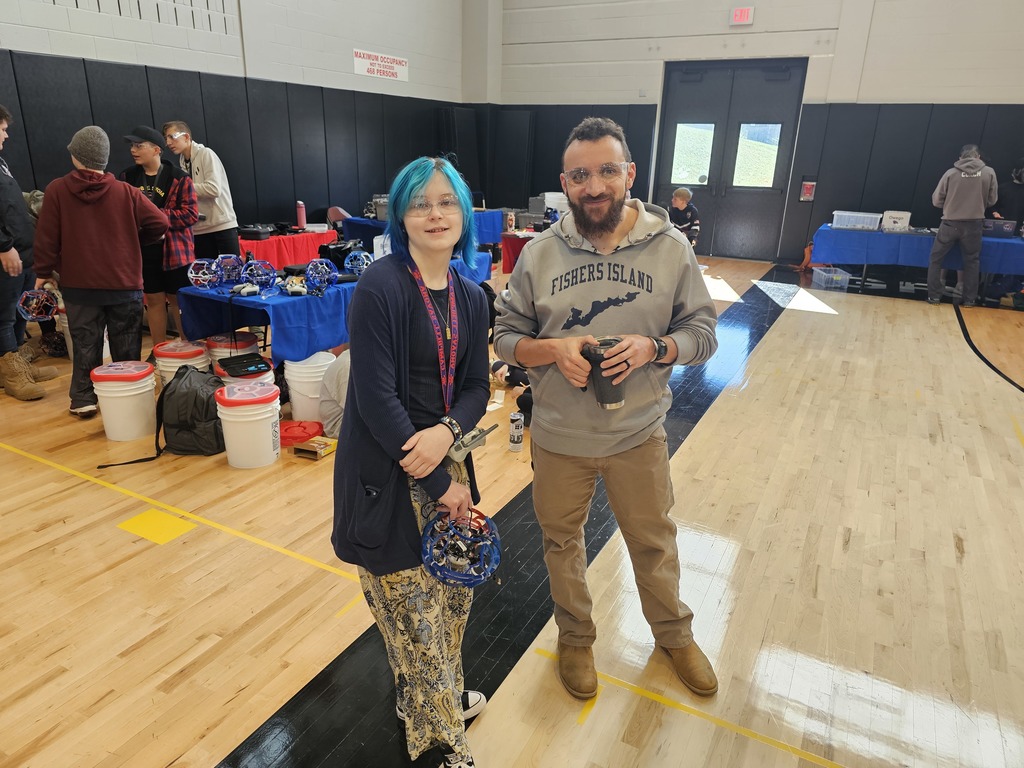 Coach and student posing for picture, one holding a drone.