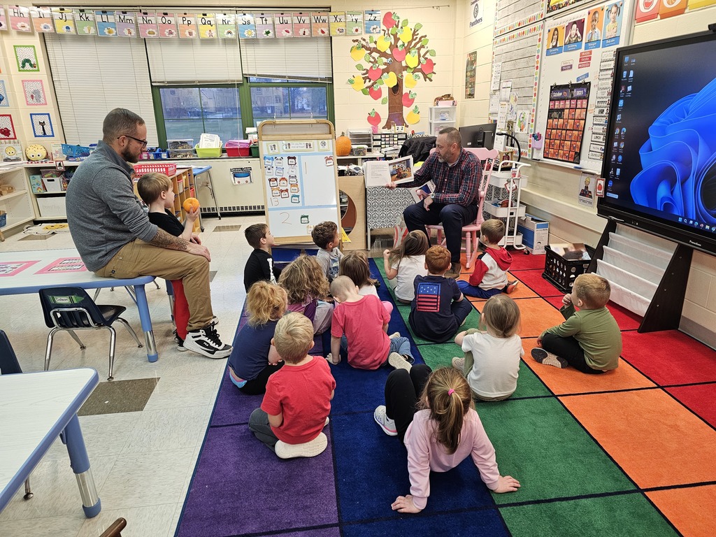 PreK students sitting on rug while adult in flannel shirt reads a story to them