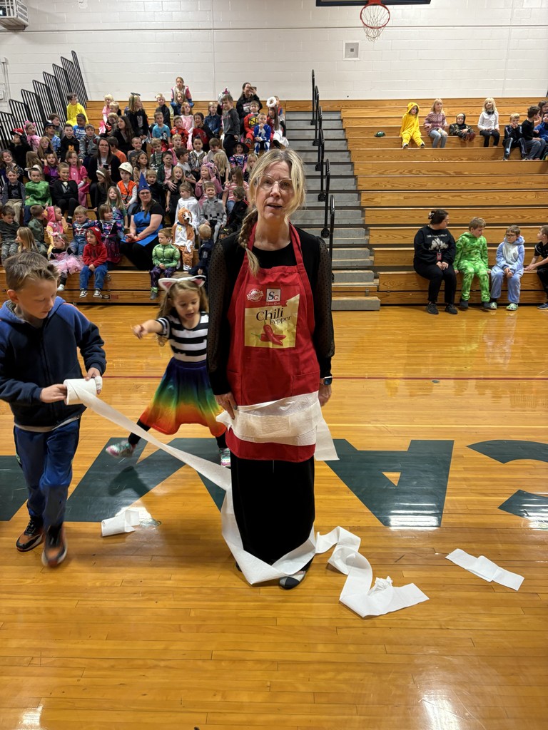 Teacher dressed up as chili spice with two students wrapping her in toilet paper.
