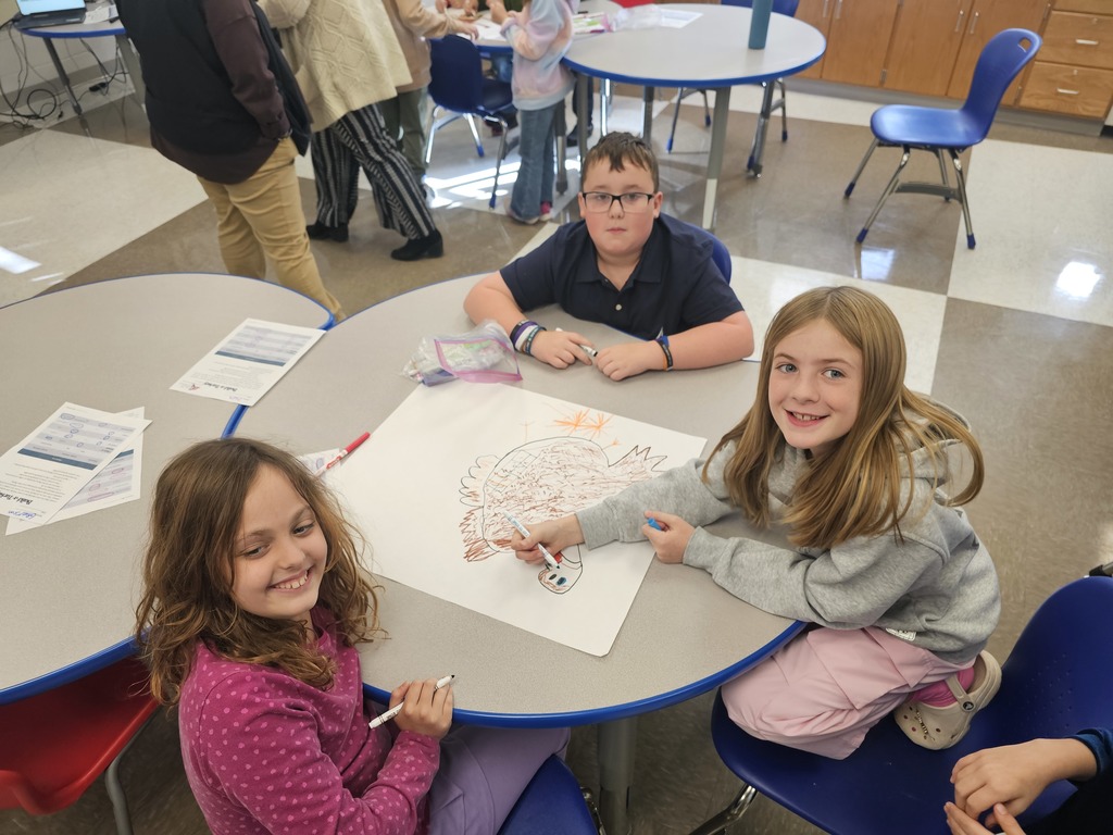 3 students at table collaborating together to draw a turkey while posing for the camera