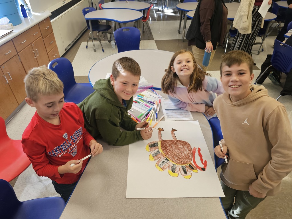 4 students at table collaborating together to draw a turkey while posing for the camera