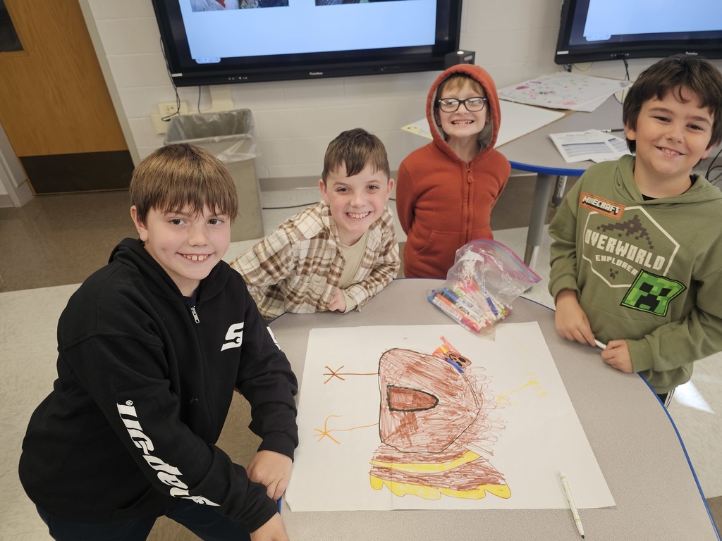 4 students at table collaborating together to draw a turkey while posing for the camera