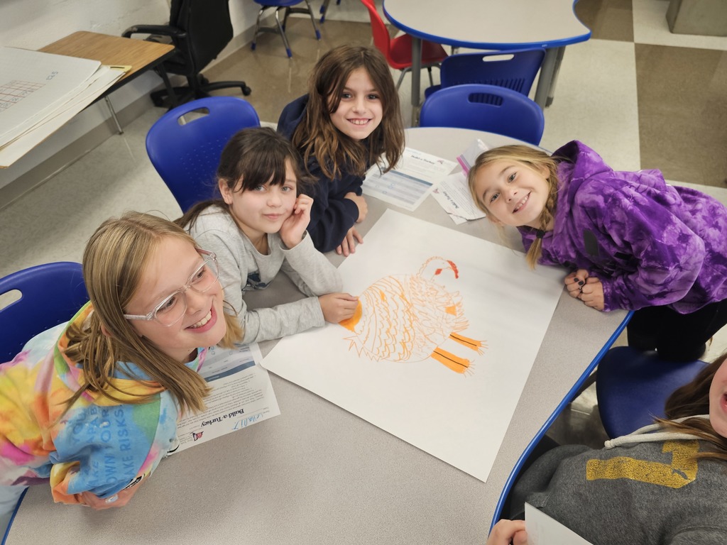 3 students at table collaborating together to draw a turkey while posing for the camera