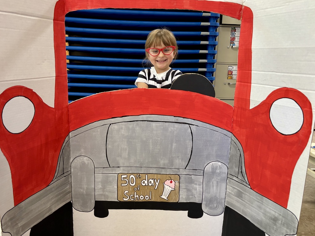 Student posing pretending to drive a 50's red car.