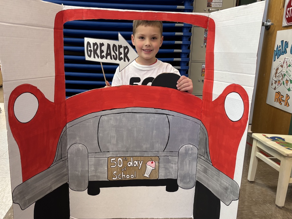 Student posing pretending to drive a 50's red car.