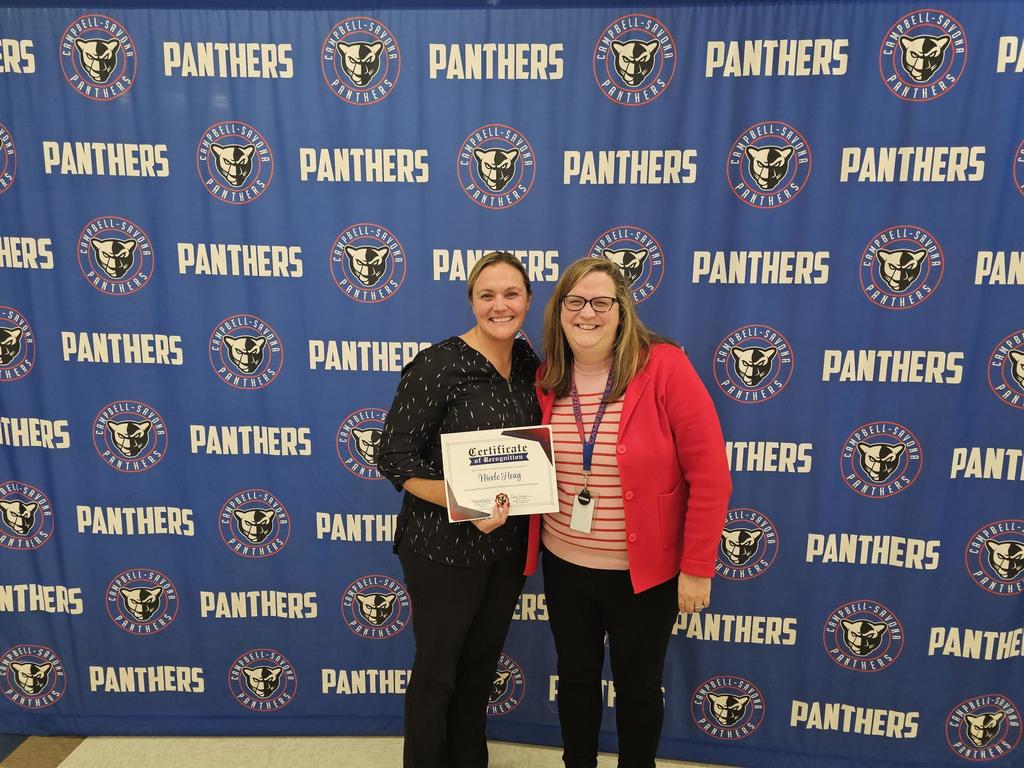 Teacher and school board president posing in front of banner,
