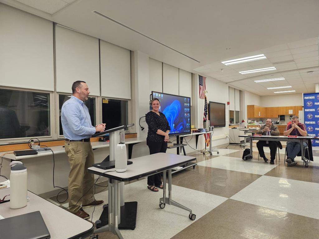 Supt standing at podium next to teacher in front of the boe
