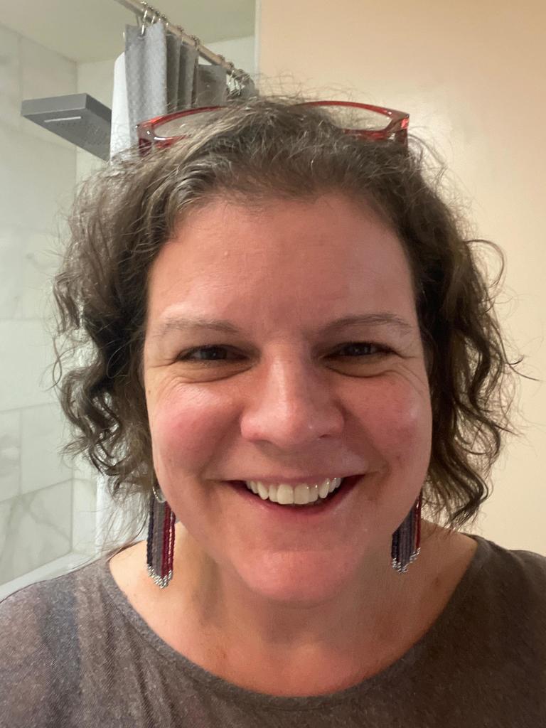 Headshot picture of girl with smile, earings and glasses set in her hair.