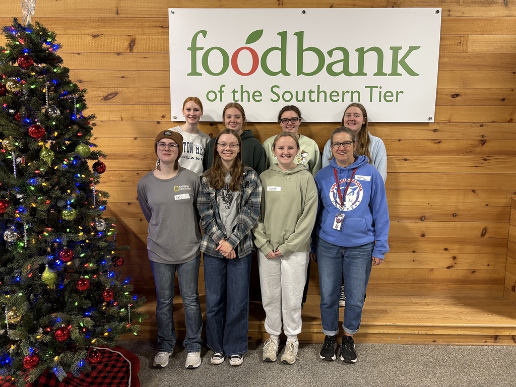 NHS students posing as a group in front of a Foodbank sign with a christmas tree next to them.