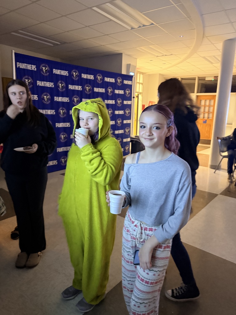 two students standing drinking hot chocolate, one wearing a grinch costume