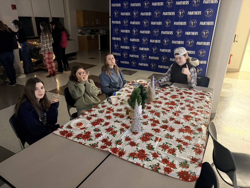 4 students sitting at table with holiday table cloth making faces at the camera