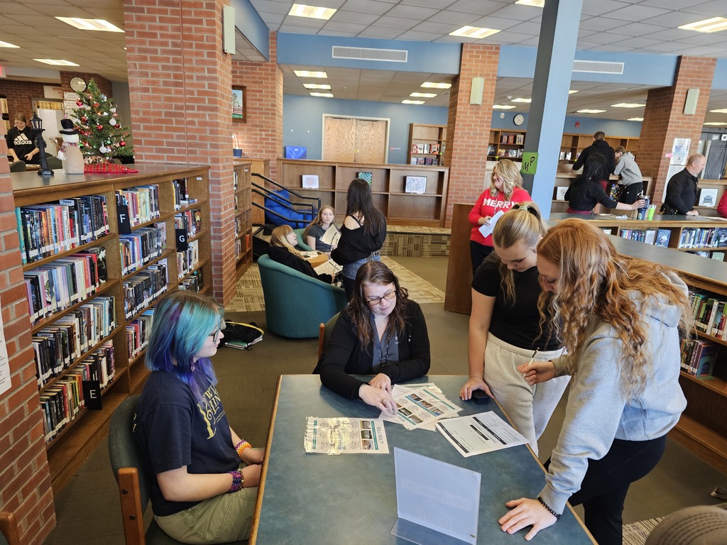 Students standing around table looking at items to budget for simulation