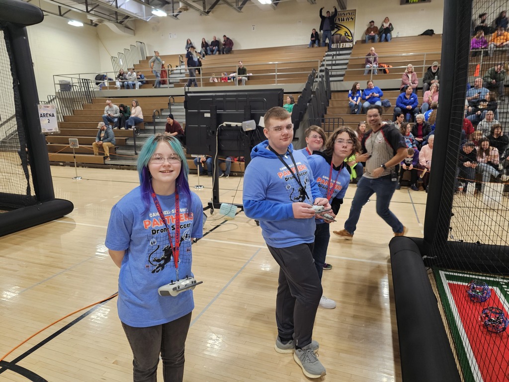 Students posing for picture in drone shirts with referee photo bombing the picture