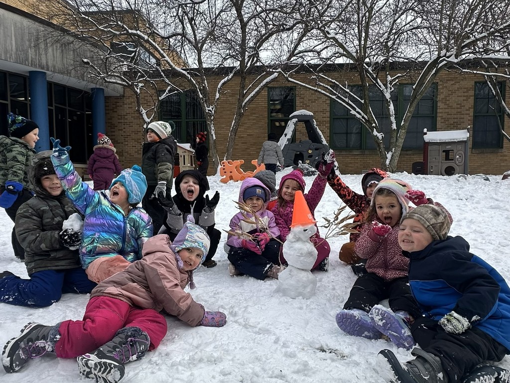 Group photo of students sitting in the snow with a snowman smiling