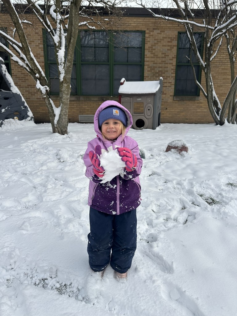 Students in purple coat and gloves holding a snowball smiling