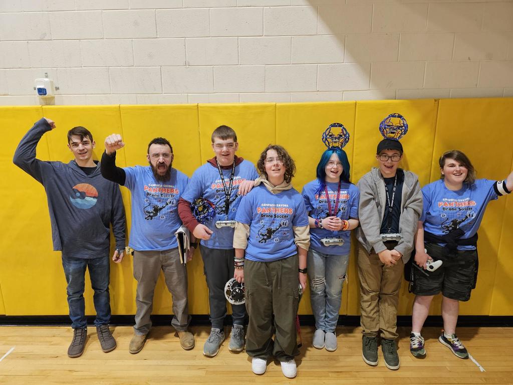 Drone soccer team posing in front of yellow matts holding controllers and drones.