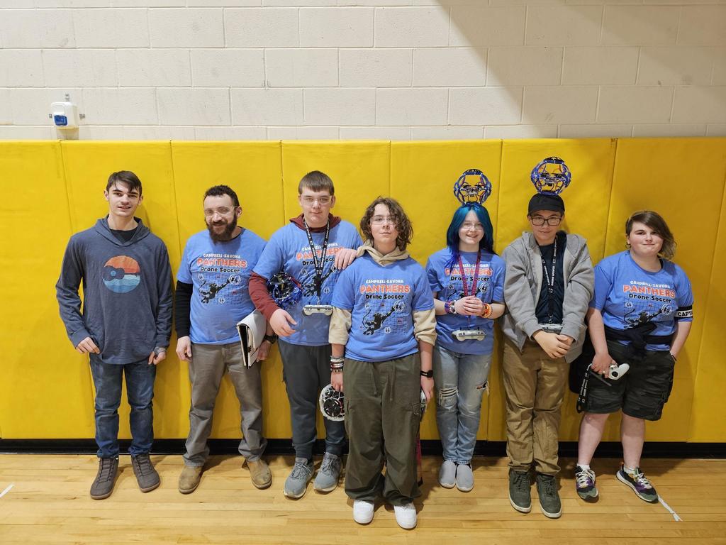 Drone soccer team posing in front of yellow matts holding controllers and drones.