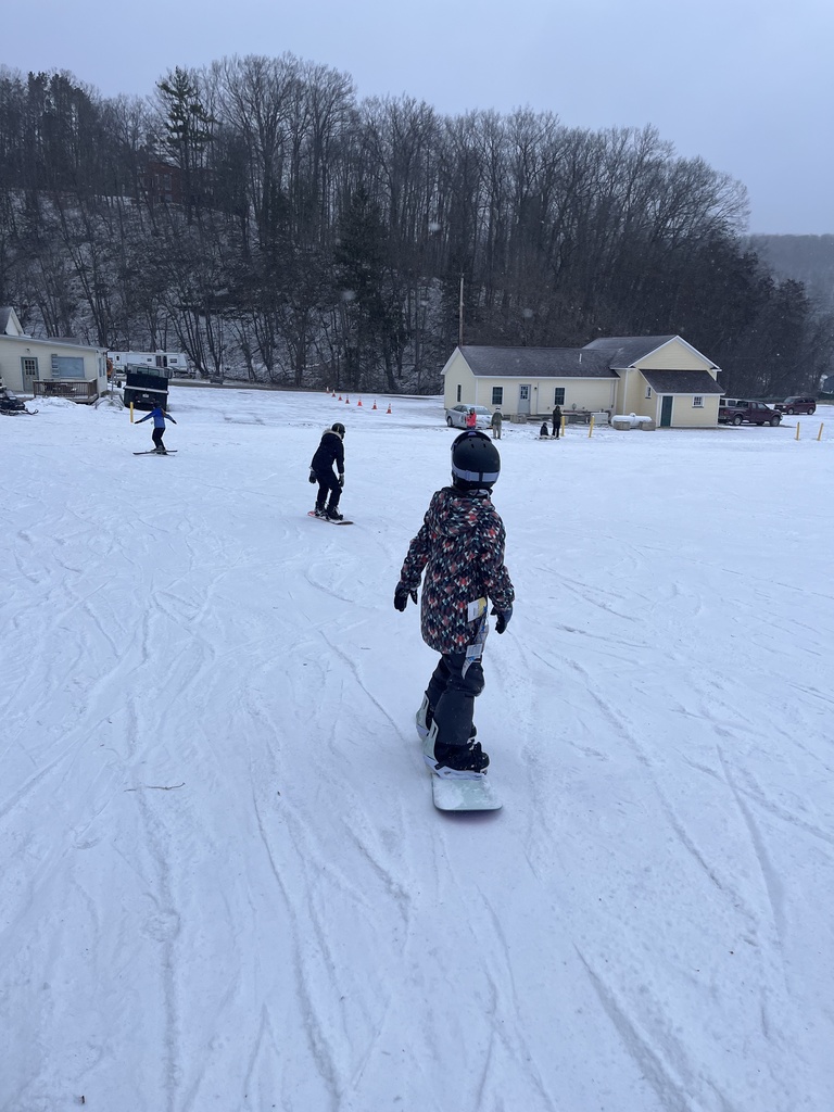 Student standing on his snow board in the snow riding it down the hill