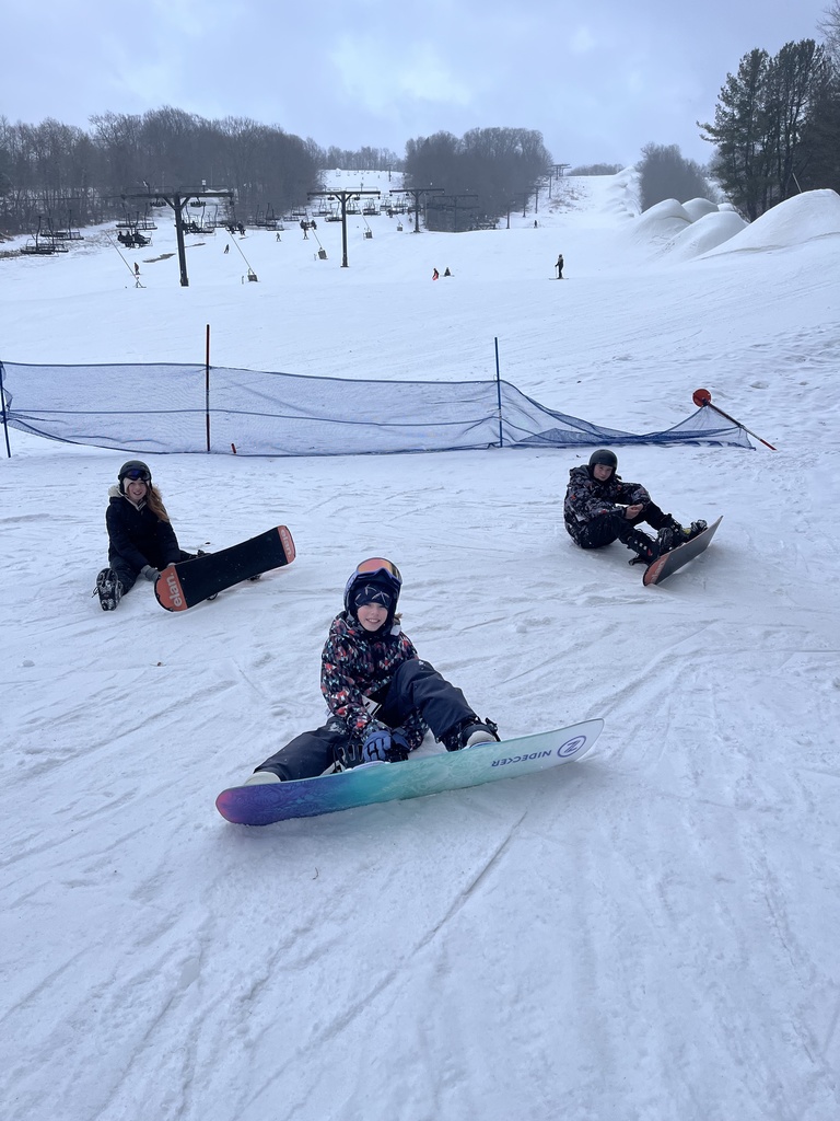 3 students siting with snowboards posing in the snow for a picture