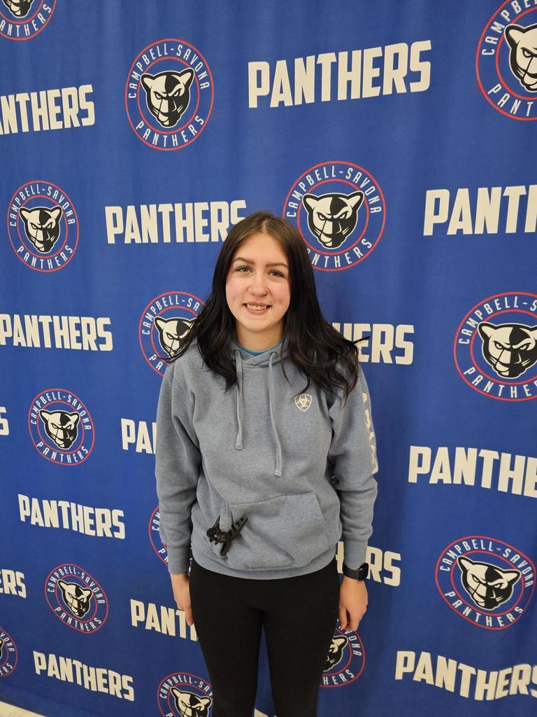 Student posing in front of panther banner with black hair and gray sweatshirt smiling