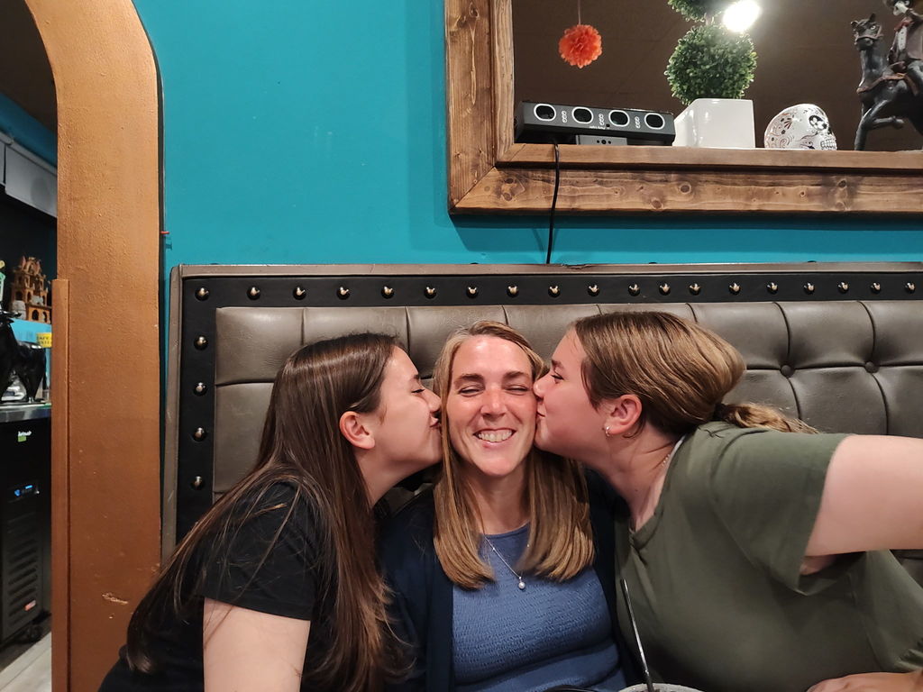 two daughters kissing mom on the cheek,