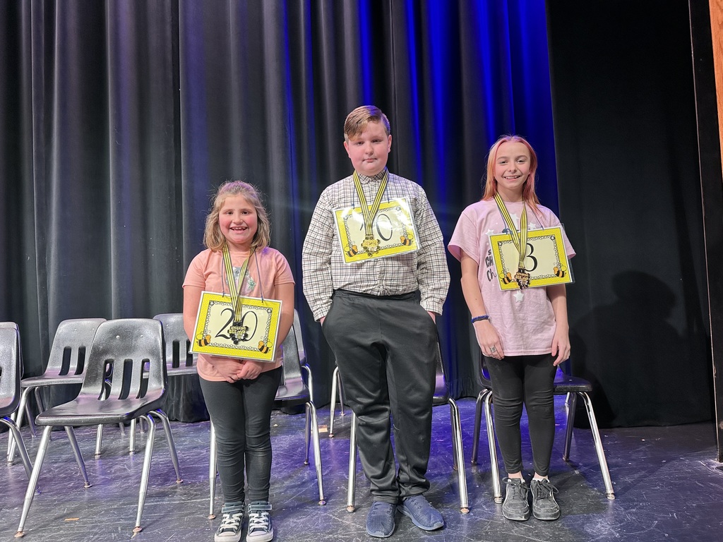 Three winners at the spelling bee standing on stage with awards