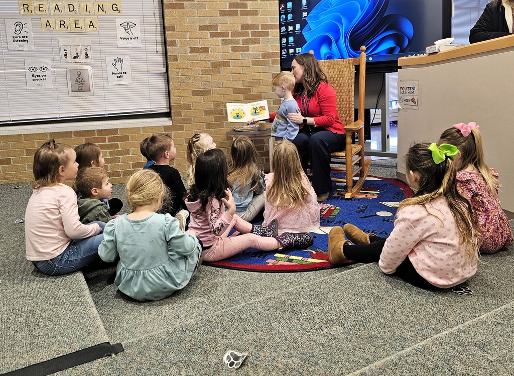 Principal reading book to students sitting on a rug