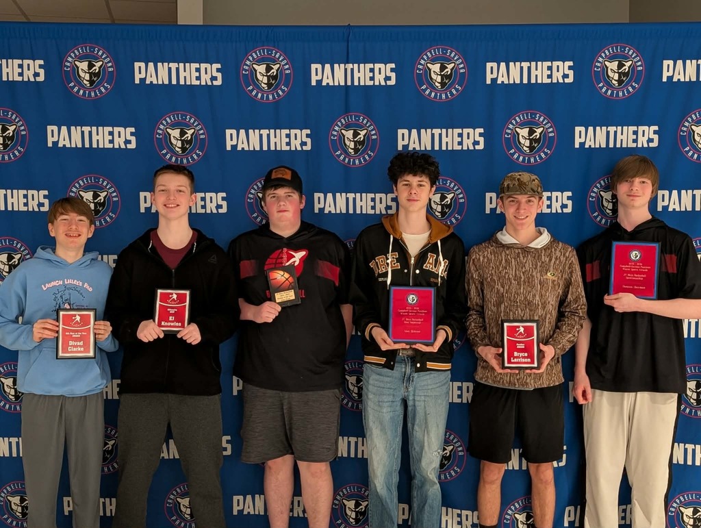 Basket ball players in front of banner holding awards