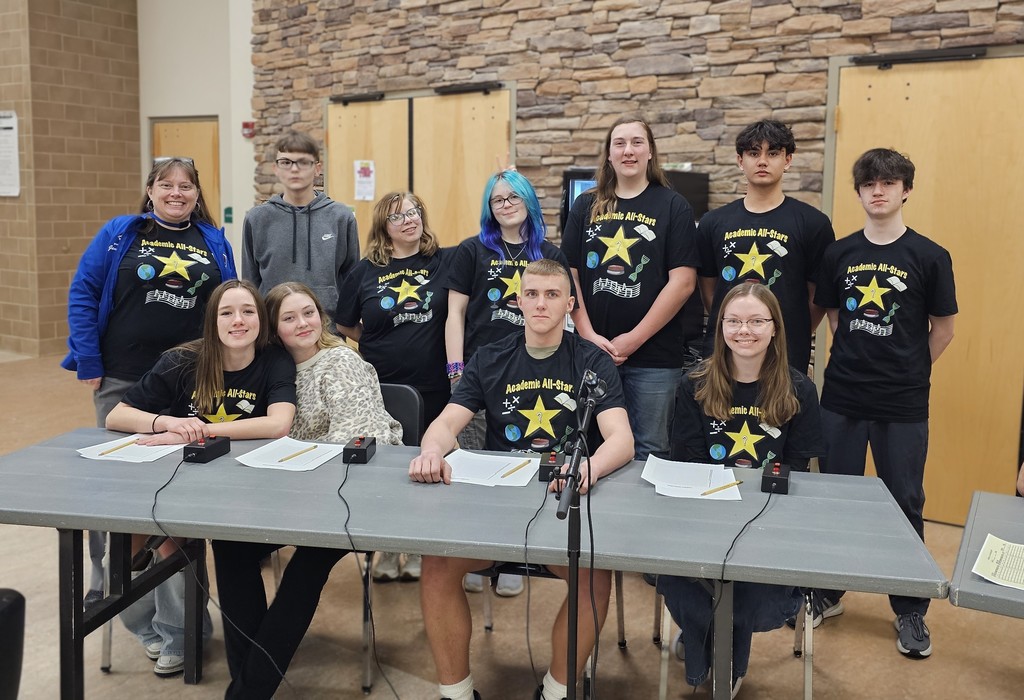 Academic Allstars posing at table with tshirts with stars on them with the coach in the left smiling
