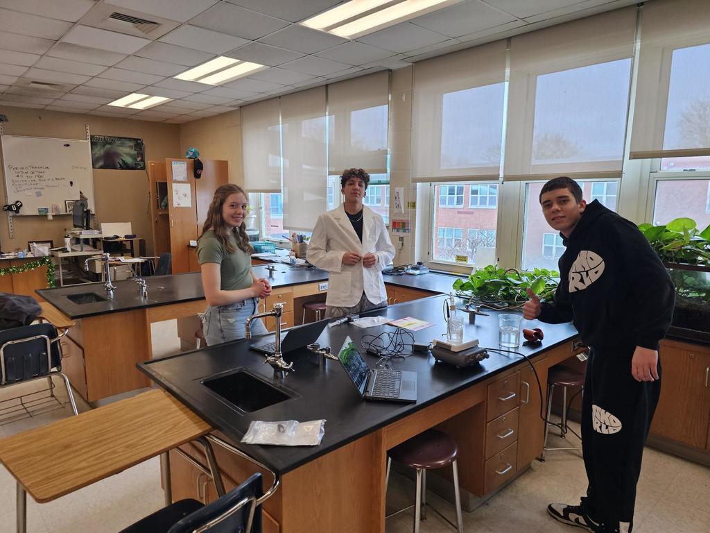 3 students standing around science equipment in class