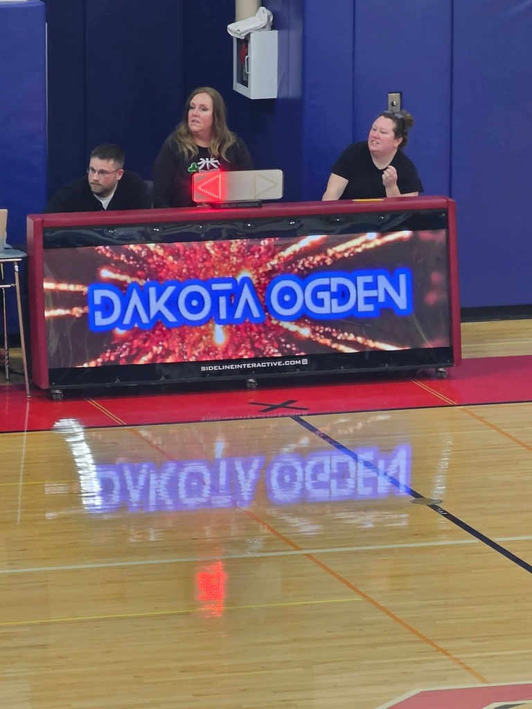 Banner table in gymnasium with 4 people sitting at it - gives name of senior