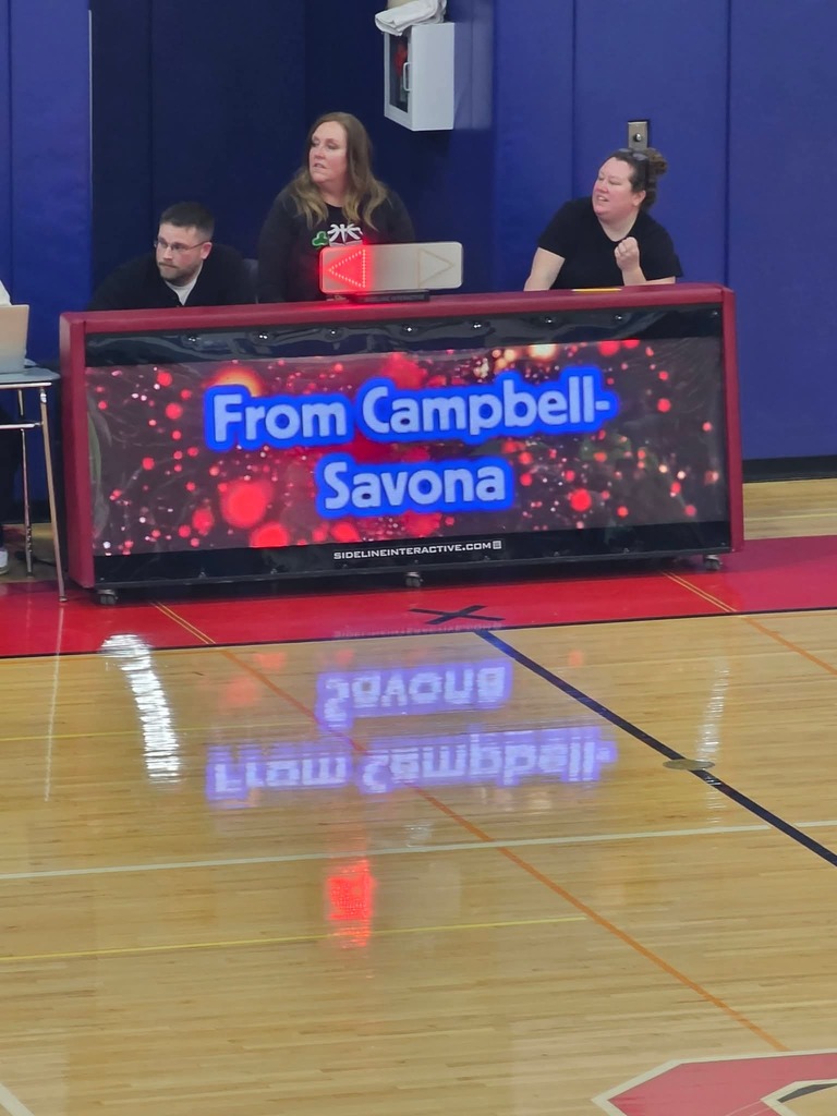 Banner table in gymnasium with 4 people sitting at it - Says Campbell Savona