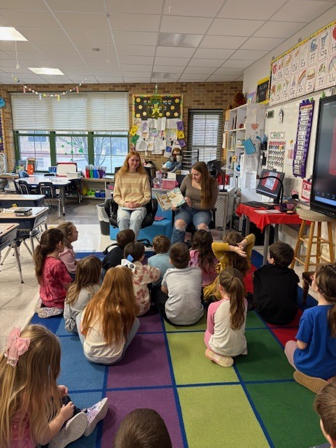 2 NHS students reading book to elementary students
