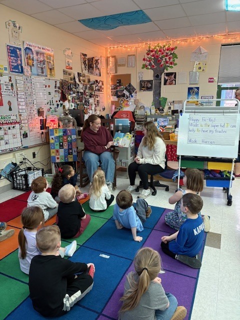 2 NHS students reading book to elementary students, holding book open in front of them
