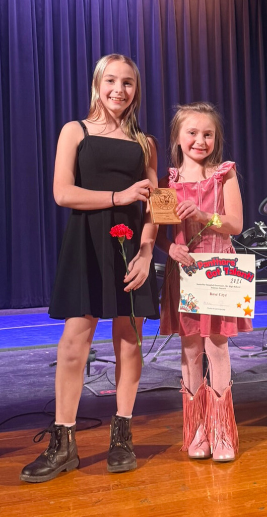 Two students standing on stage with flowers in hand from talent show.
