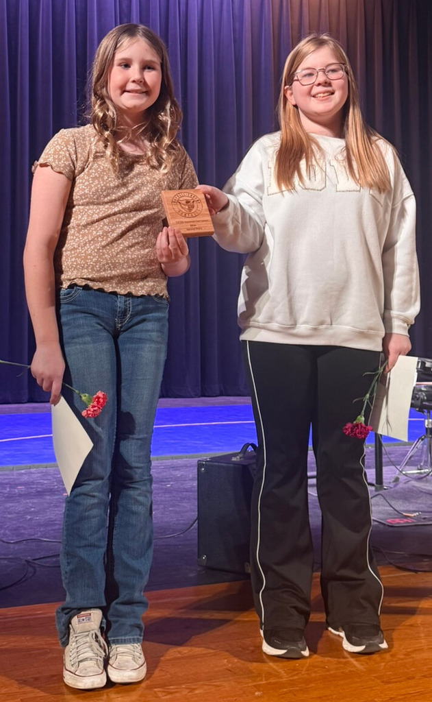 Two students standing on stage with flowers in hand from talent show.