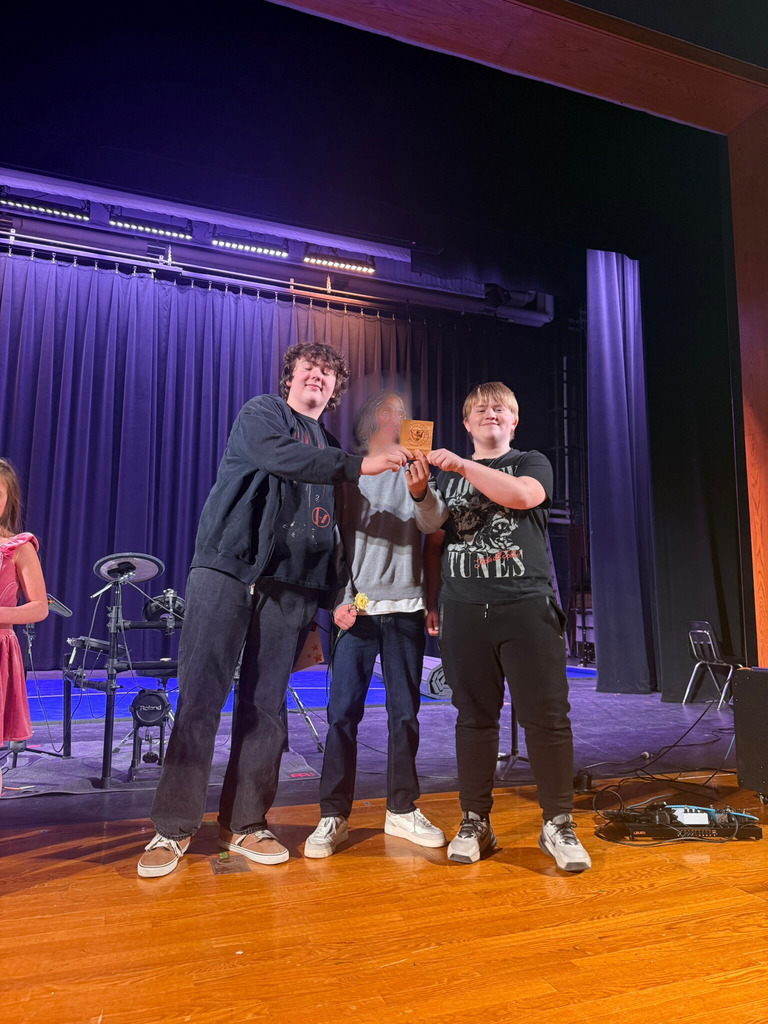 Three students standing on stage at talent show holding plaques