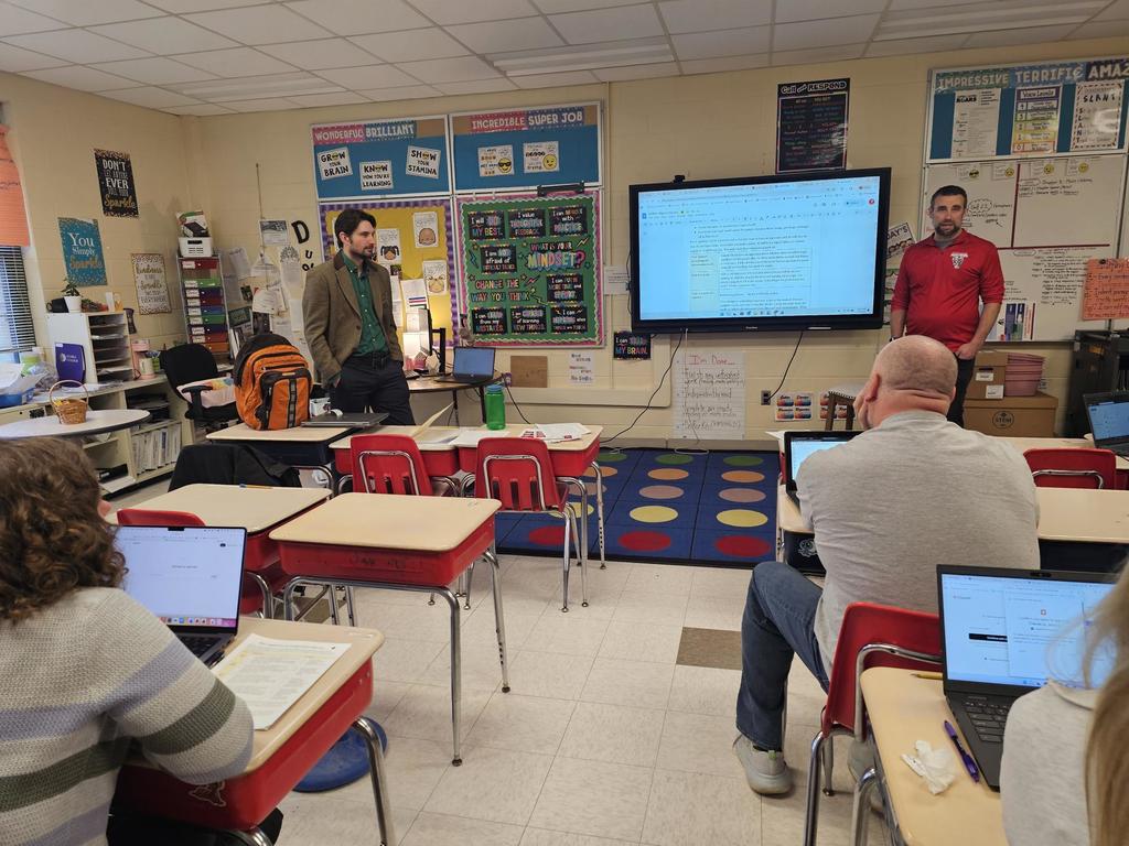 Two adults standing in front of classroom teaching.