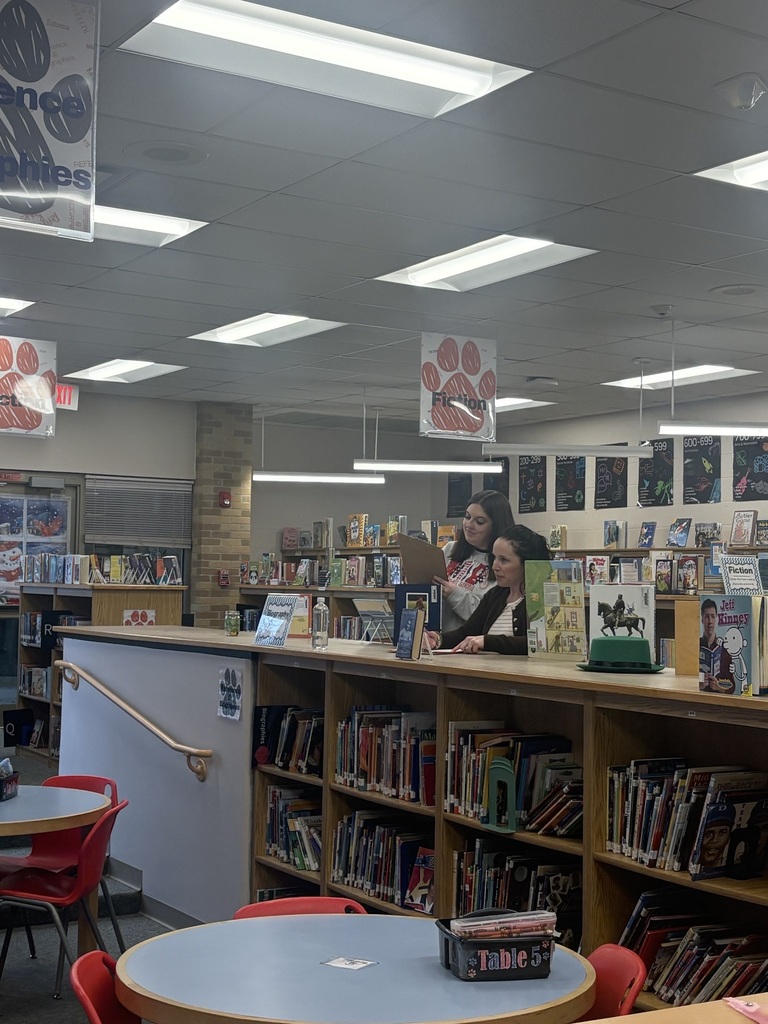 Two teachers standing in library looking at clipboard together