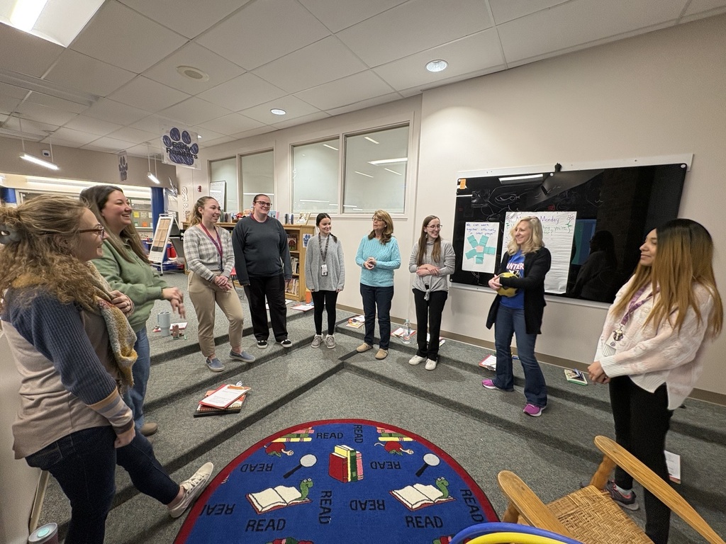 Teachers standing in a circle in hte library facing each other