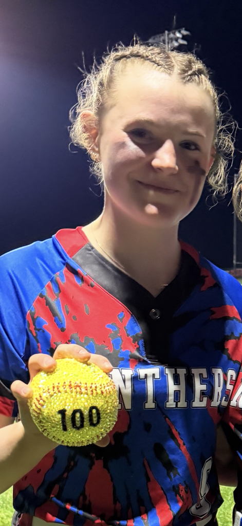 Student in softball uniform holding softball with the #100 on it