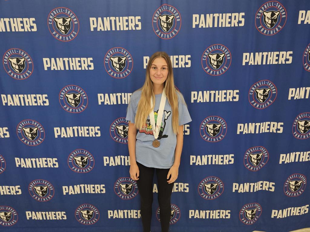 Student wearing a medal standing in front of the panther banner