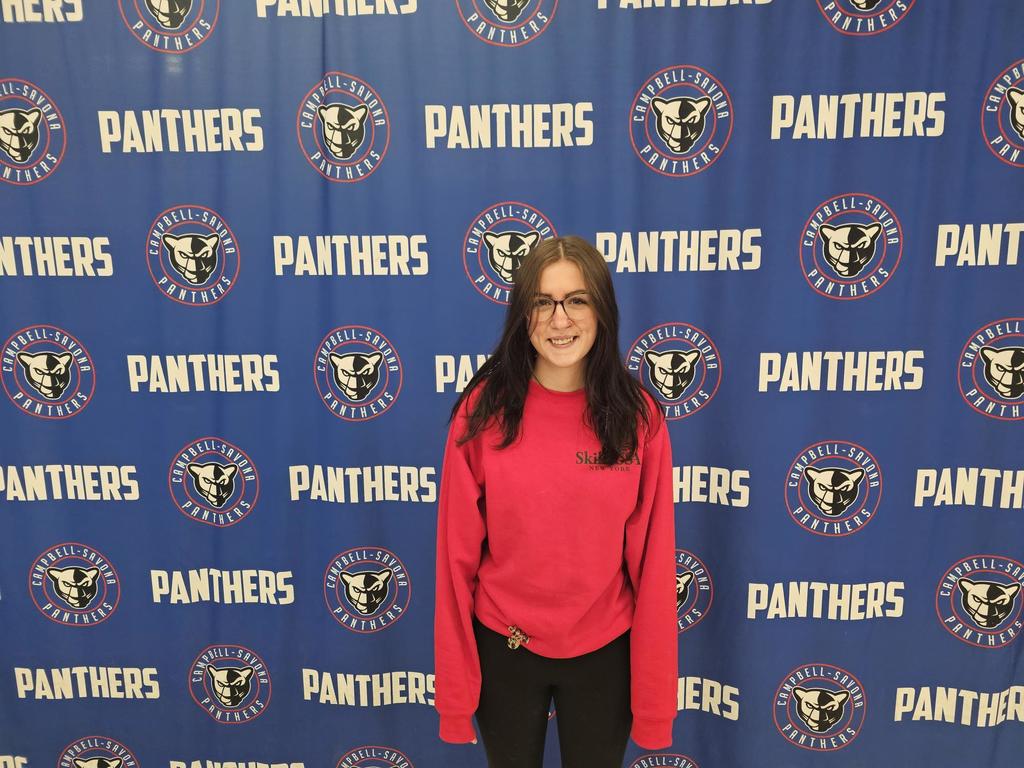 Student in red shirt standing in front of panther banner
