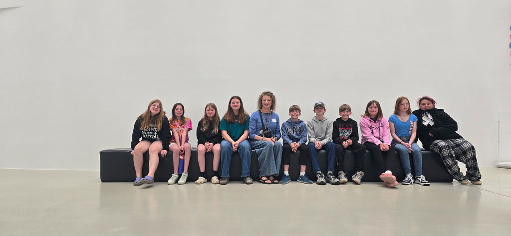 Group photo of students sitting wtih white background and teacher in the middle