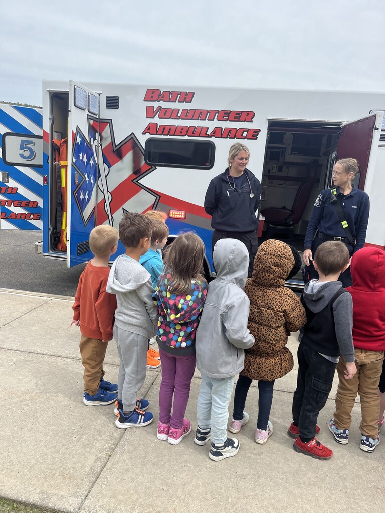 STudents carwded around ambulance with two adults in blue uniforms