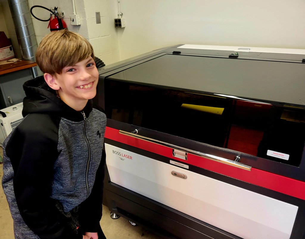 Student smiling standing in front of a laser engraver