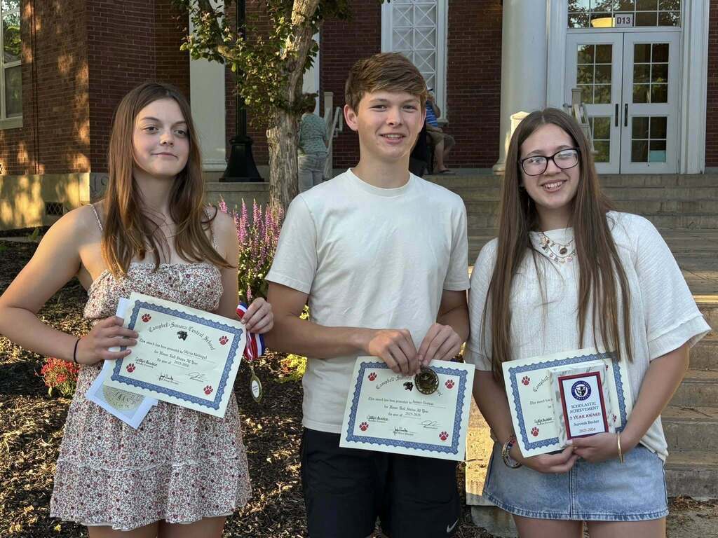 3 students holding awards standing outside of the school