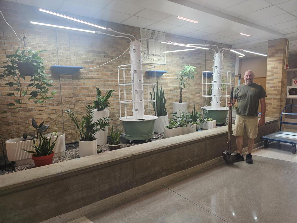 Teacher with shovel standing in front of hydroponic garden