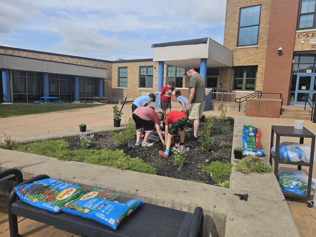 STudents planting garden with teacher watching them
